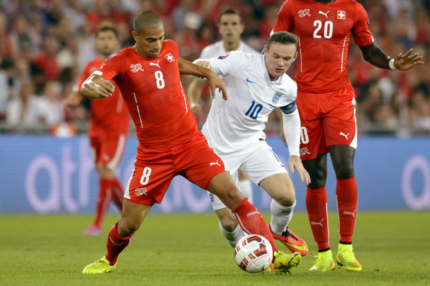 Gökhan Inler (s číslom 8) je aj bývalým kapitánom Švajčiarska. Na snímke bojuje o loptu s hráčom Anglicka Waynom Rooneym.