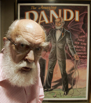 James Randi pózuje pred plágátom vo svojom dome.