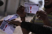 Palestínčania ukazujú na kameru letáky zhadzované izraelským dronom varujúce ľudí, aby sa nevzďaľovali z tzv. žltej zóny v meste Chán Júnis, na juhu Pásma Gazy.