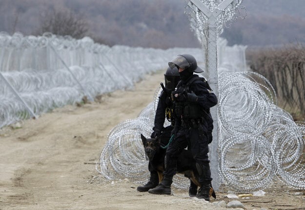 Českí  policajti stoja vedľa dvoch radov ostnatého drôtu na hraniciach Grécka a Macedónska.