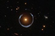 Galaxia Kozmická podkova. Novoobjavená ultramasívna čierna diera sa nachádza v strede oranžovej galaxie. Ďaleko za ňou sa nachádza modrá galaxia, ktorá je hmotnosťou oranžovej galaxie v popredí deformovaná do tvaru podkovy.