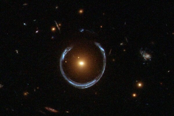 Galaxia Kozmická podkova. Novoobjavená ultramasívna čierna diera sa nachádza v strede oranžovej galaxie. Ďaleko za ňou sa nachádza modrá galaxia, ktorá je hmotnosťou oranžovej galaxie v popredí deformovaná do tvaru podkovy.