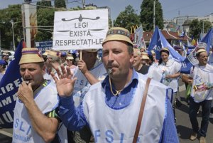 Rumunskí učitelia protestujú za vyššie platy. V pozadí je transparent s nápisom "Zákony existujú, rešpektujte ich".