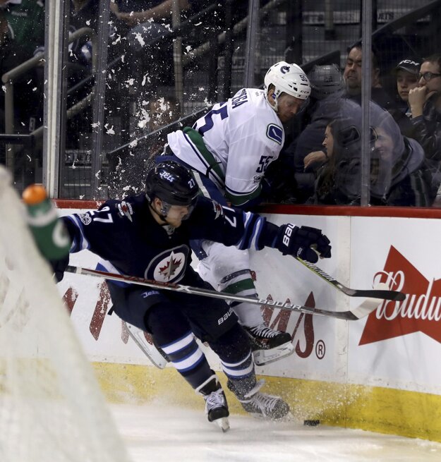 Nikolaj Ehlers z Winnipegu (vľavo) vráža na mantinel hráča Vancouveru Alexa Biegu.