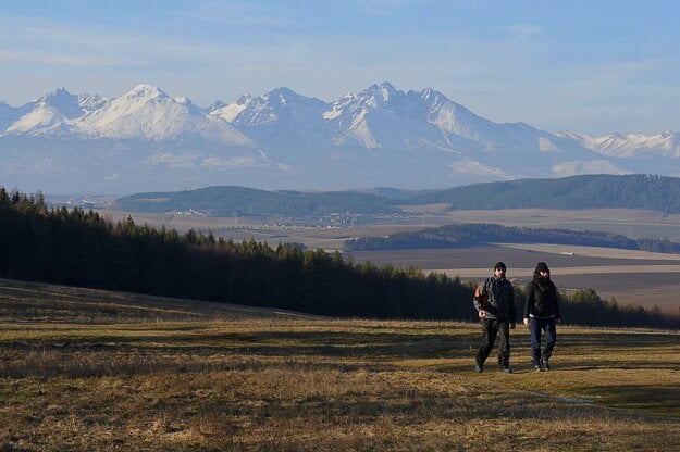 Tourists walk through a meadow near the Tomášovský výhľad viewpoint in the Slovenský raj national park. A panorama of the High Tatras can be seen in the background.